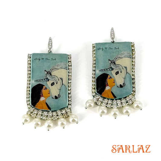 Earrings with artistic depiction of a woman and a unicorn on a blue background, featuring the brand 'SARLAZ'.