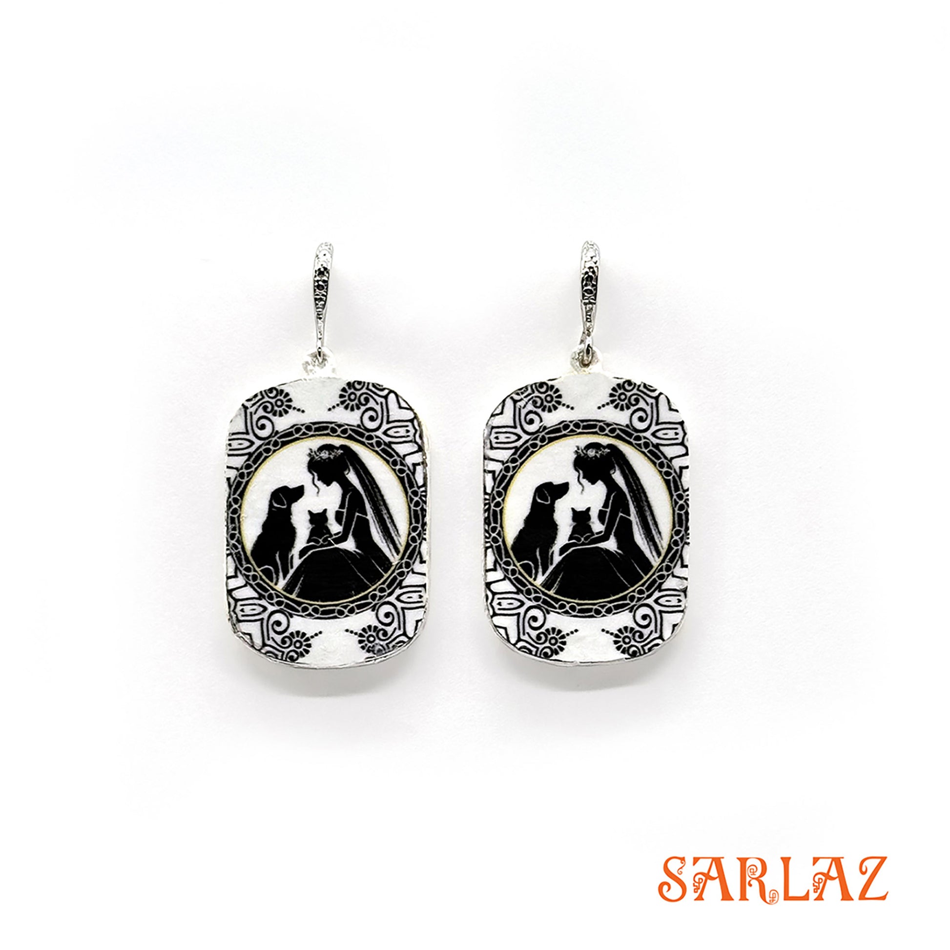 Pair of earrings with a black and white design of a bride with her cat and dog, branded 'SARLAZ', on a white background.