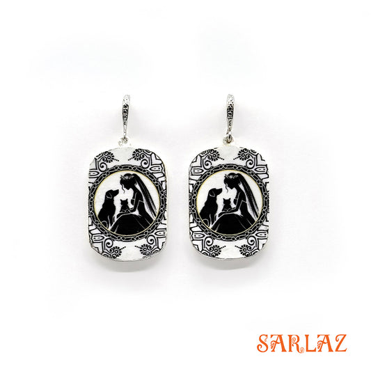 Pair of earrings with a black and white design of a bride with her cat and dog, branded 'SARLAZ', on a white background.