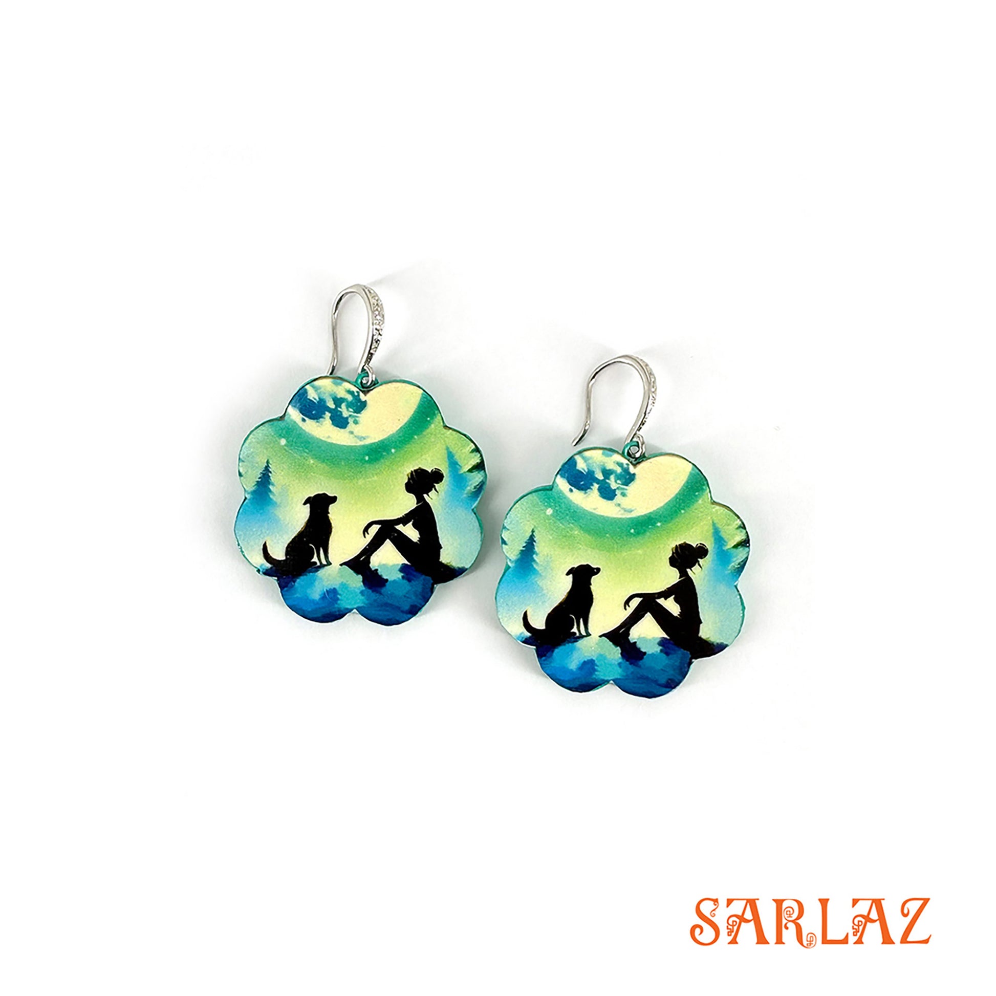A pair of earrings, framed in a moonlit palette, this design features a girl and her fur kid soaking in the evening calm. Crafted on wood in a floral silhouette, it marks a peaceful, emotional pause branded 'SARLAZ'.