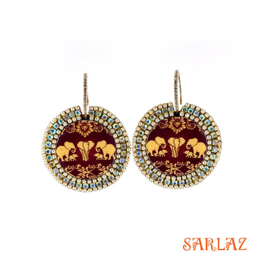 Pair of earrings with elephant family design on maroon pattern background, featuring the brand 'SARLAZ'.